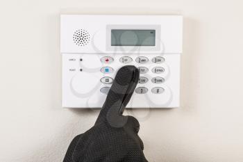 Hand wearing black glove touching alarm system panel