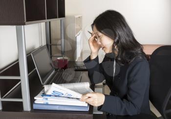 Professional Mature Asian woman mentally preparing for income taxes with tax form booklet, calculator, coffee cup, glasses and computer on desk