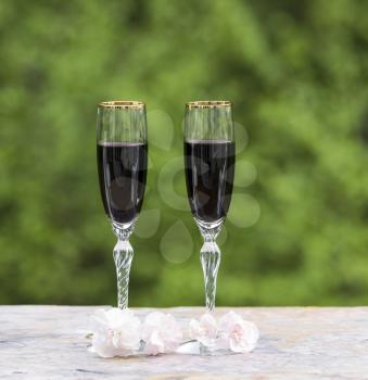 Photo of red wine in glasses with late spring pink flower on bright green background