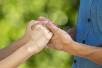 closeup horizontal photo of a young adult couple holding hands with blurred out green woods in background