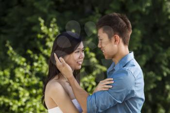 Horizontal photo of a young couple looking into their lovers eyes with green trees in background