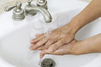 Horizontal photo of female hands finishing cleanup with running water and bathroom sink in background