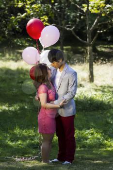 Vertical photo of young adult couple dressed in formal attire having fun outdoors with several balloons behind them  