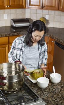 Vertical photo of mature woman putting top of cooked winter melon back on while placed in dinner plate next to cooking kettle on stove top 