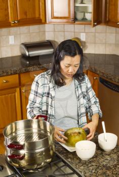 Vertical photo of mature woman working with cooked winter melon on dinner plate next to cooking kettle on stove top 