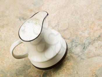 Angled photo of pitcher filled with almond milk sitting on stone counter top 