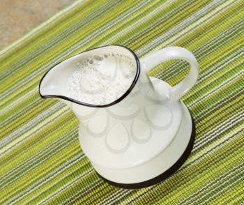 Angled photo of soy milk in white pitcher with green table cloth underneath 