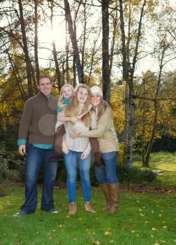 Vertical photo of family standing in front of trees, with sunlight coming through, during a nice day in the fall season