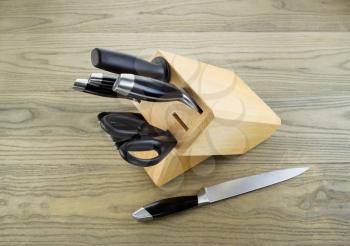 Photo of kitchen knives, scissors and sharpener in wooden holder with single knife lying on aged white ash boards