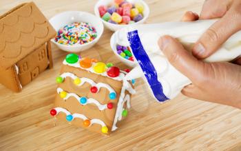 Horizontal photo female hands making Gingerbread houses with ingredients and natural bamboo wood underneath  