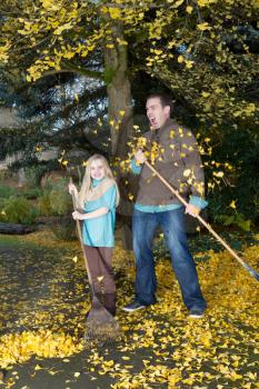 Vertical photo of dad showing strong emotion as the leaves just keep falling from the tree while he is raking them up with his young daughter