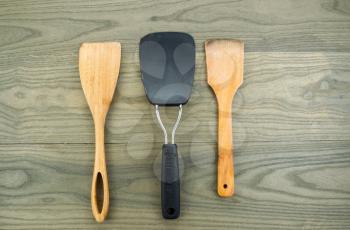 Horizontal photo of three kitchen spatulas, two of them wooden, on aged white oak boards 