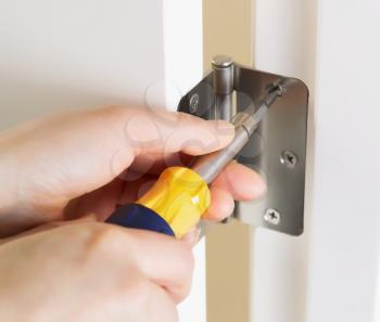 Photo of female hands, with screwdriver, tightening door hinge