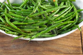 Horizontal photo of freshly cooked green beans in white bowl on black walnut serving board