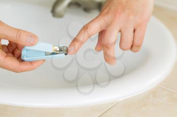 Horizontal photo of female hands trimming fingernails in bathroom with sink and counter top in background 