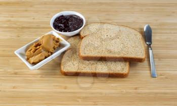 Horizontal photo of peanut butter and jelly sandwich ingredients and spread knife with natural bamboo cutting board underneath