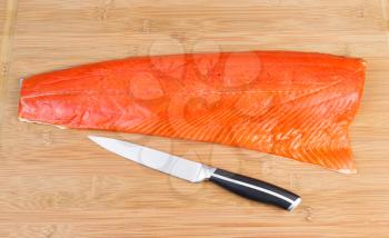 Horizontal photo of fresh Wild Red Salmon with sharp cutting knife on natural bamboo board