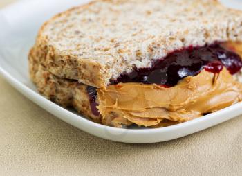 Closeup horizontal photo of a peanut butter and jelly sandwich cut in half, inside white plate on textured table cloth underneath