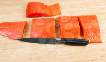Horizontal photo of fresh Wild Red Salmon pieces from Fillet with cutting knife in front and bamboo board underneath 
