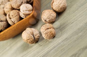 Angled horizontal photo of whole walnuts lying on faded wood with additional nuts and wooden bowl in background