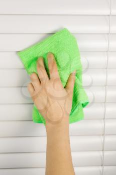 Vertical photo of female hand cleaning window blinds with microfiber cloth