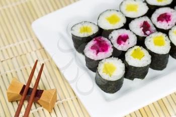 Horizontal photo of partial plate of pickled hand rolled sushi with chop sticks and holder in background and natural unstained bamboo dinner mat underneath