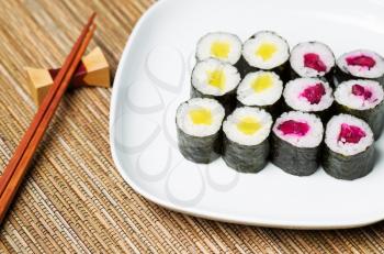 Horizontal photo of pickled sushi hand roll on white plate and chop sticks inside of holder in background with natural bamboo dinner mat underneath
