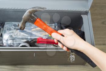 Horizontal photo of female hand taking old hammer out of toolbox with aged wooden floors in background 