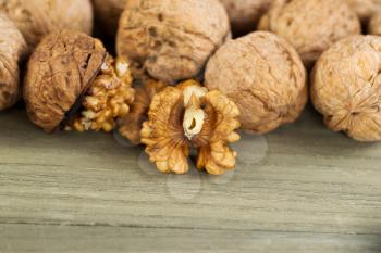 Close up horizontal photo of unshelled half of walnuts lying on faded wood with additional nuts both shelled and unshelled in background 