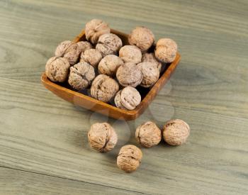 Top view photo of whole walnuts lying on faded wood with additional nuts in wooden bowl 