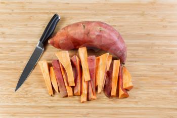 Horizontal photo of freshly cut Yams for cooking French fries with knife and bamboo cutting board