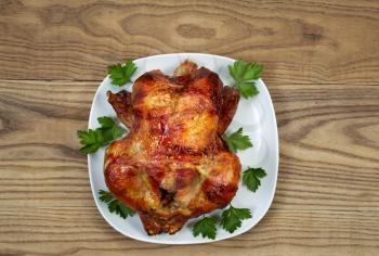 Overhead view of a freshly oven roasted whole chicken in white serving surrounded by large leaf parsley plate placed on rustic wood