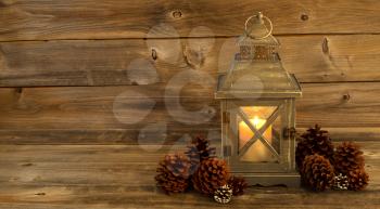 Horizontal front view of an old Asian design lantern and white candle glowing brightly inside with natural pine cones decorations on rustic wood