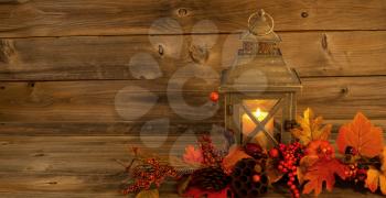 Horizontal front view of an old Asian design lantern and white candle glowing brightly inside with autumn decorations on rustic wood