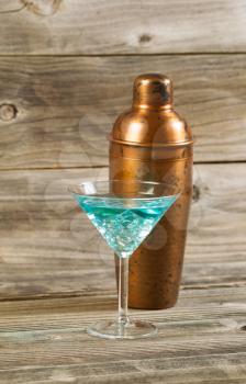 Vertical photo of a mixed drink and a metal mixer resting on rustic wood