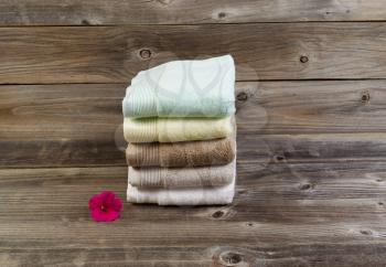 Horizontal photo of clean stacked towels and single healthy flower on rustic wood