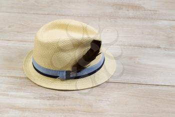 Horizontal view of straw hat with bird feather on faded white wood.  