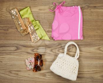 Overhead view of summer clothing and accessories placed on rustic wooden boards.  Items include cloth purse, hair clips, elastics, and waist with head bands. 