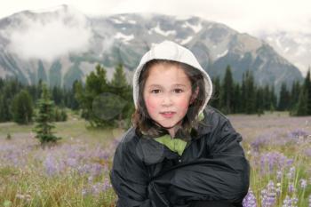 Horizontal photo of young girl, looking forward, during early spring with mountains and wild flowers in background