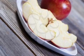 Closeup angled horizontal photo of fresh apple slices, on white plate, with whole apple and rustic wood in background  