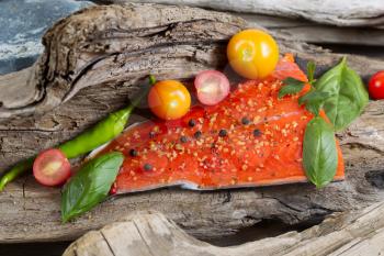 Horizontal view of raw salmon fillet, skin side down, with seasoning inside of drift wood 