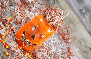 Closeup angled horizontal image of a scary orange pumpkin jar filled with shredded paper placed on rustic wooden boards 