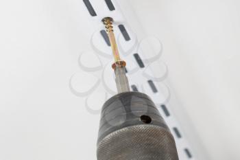 Closeup of power screwdriver putting screw into support bracket on wall with focus on head of screw