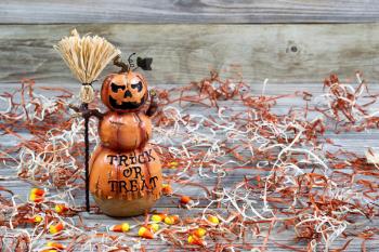 Horizontal image of a scary orange pumpkin figure holding straw broom placed on rustic wooden boards 