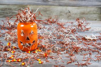Horizontal image of a scary orange pumpkin jar filled with shredded paper placed on rustic wooden boards 