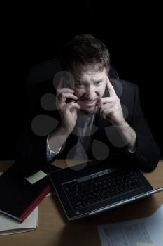 Vertical image of business man, expressing anger while on his cell phone, working late with black background 