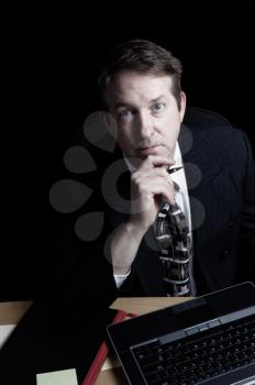 Vertical image of business man, looking forward, working late with black background 