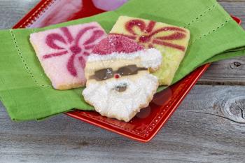 Close up of Christmas sugar cookies on green napkin and red plate with rustic wood underneath 