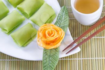 Close up top view horizontal image of Chinese Durian fruit dessert rice cakes, yellow decoration rose, and green tea with natural bamboo place mat 