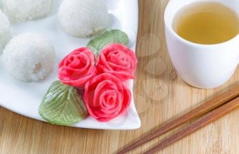 Close up horizontal image of Chinese sweet sticky rice balls, in background, red decoration roses, and green tea with natural bamboo background  